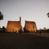 Luxor Temple at sunset with illuminated pylons and palm trees in Luxor, Egypt