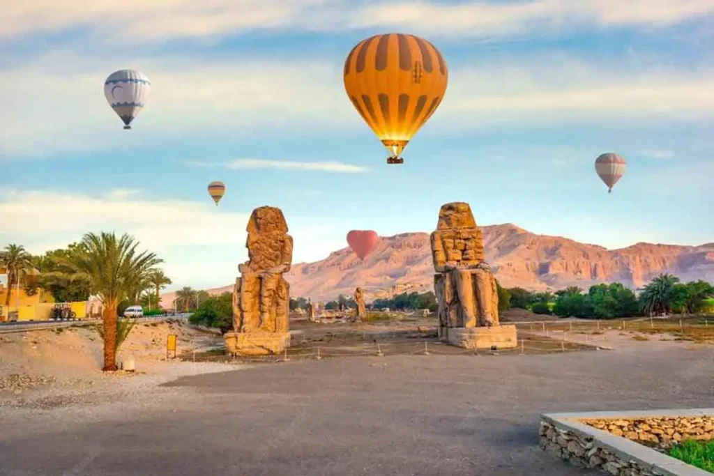 Hot air balloon flying over ancient statues in Luxor, Egypt at sunrise.